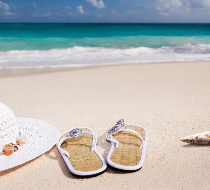 Sandstrand med solhat, sandaler og en konkylie